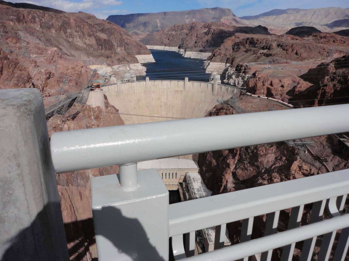 White handrails on a pedestrian bridge. The Hoover Dam is visible in the background.