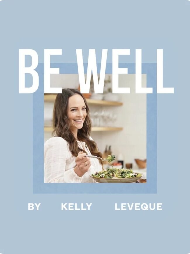 Woman holding a salad, smiling inside a kitchen. Text reads "BE WELL by Kelly Leveque" on a blue background.
