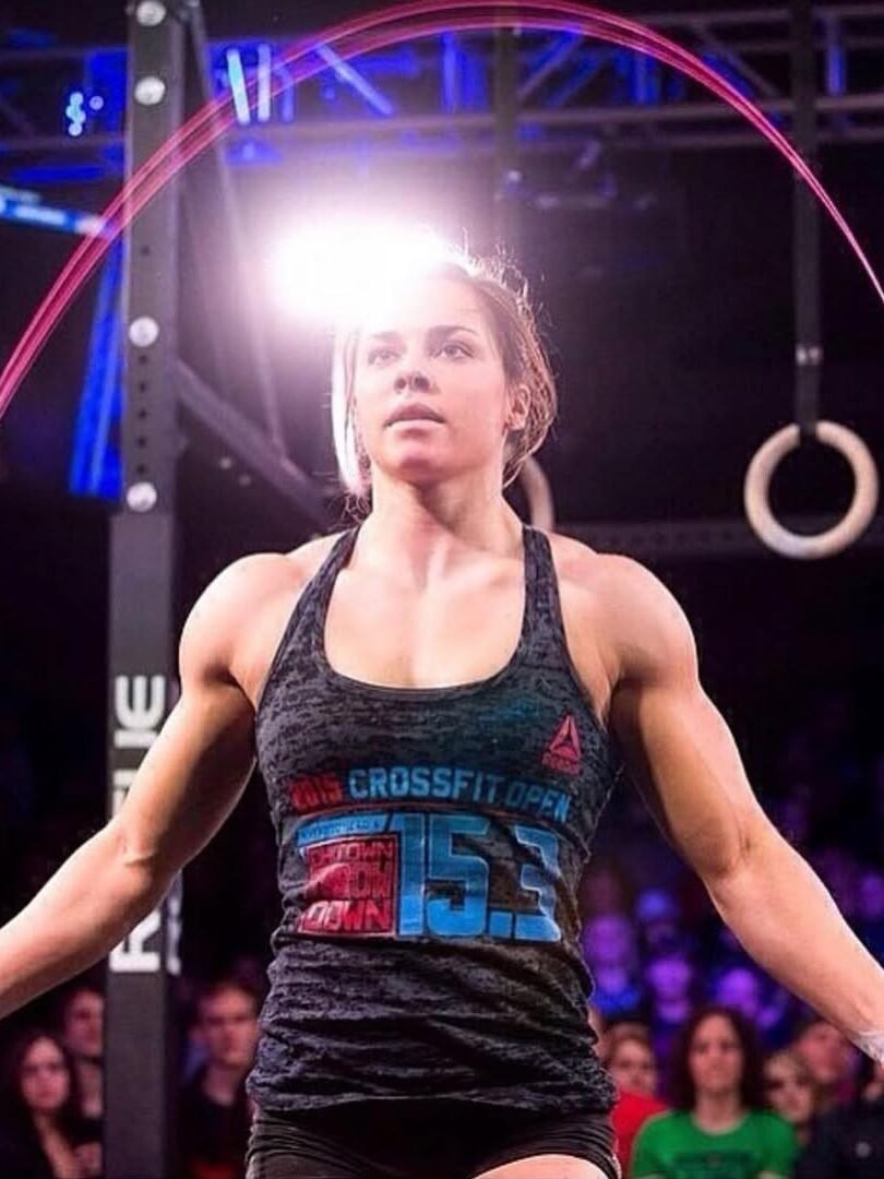 A person is intensely jumping rope in a gym with a focused expression. They are wearing a tank top and surrounded by spectators and gym equipment.