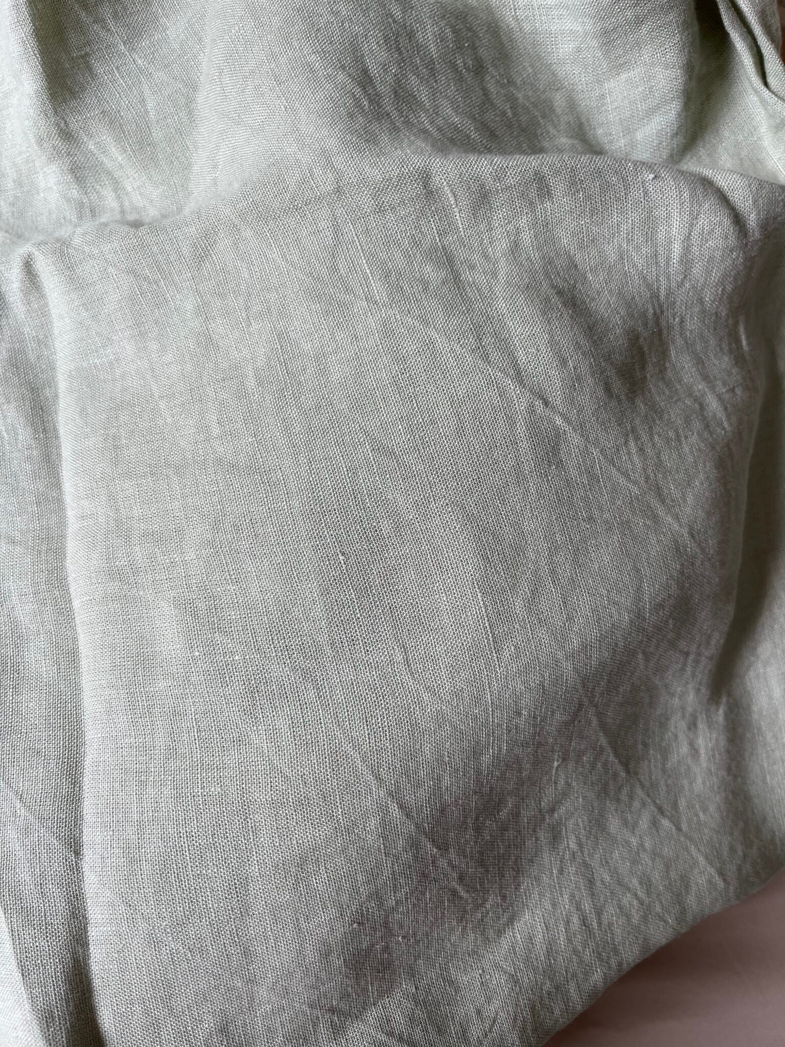 Close-up of light grey, wrinkled linen fabric with visible texture and weave pattern.