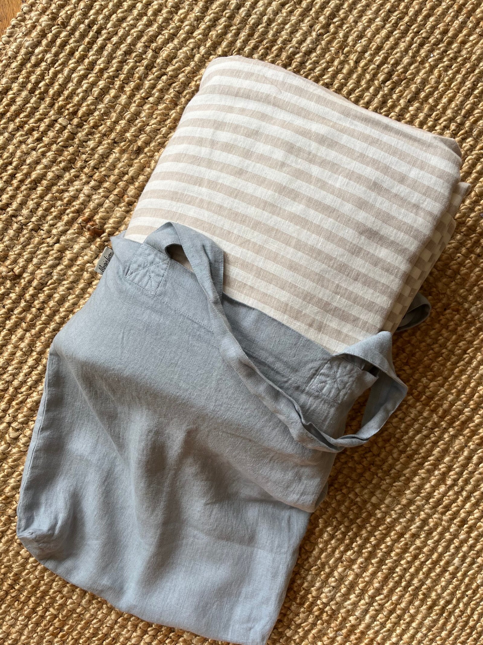 Folded beige and white striped fabric with a blue cloth bag on a woven mat background.
