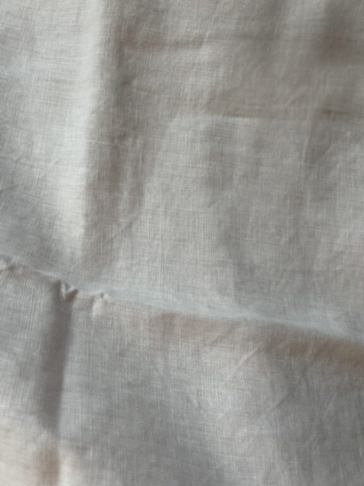 A close-up of a light-colored, slightly wrinkled fabric with visible weave texture and minor creases.