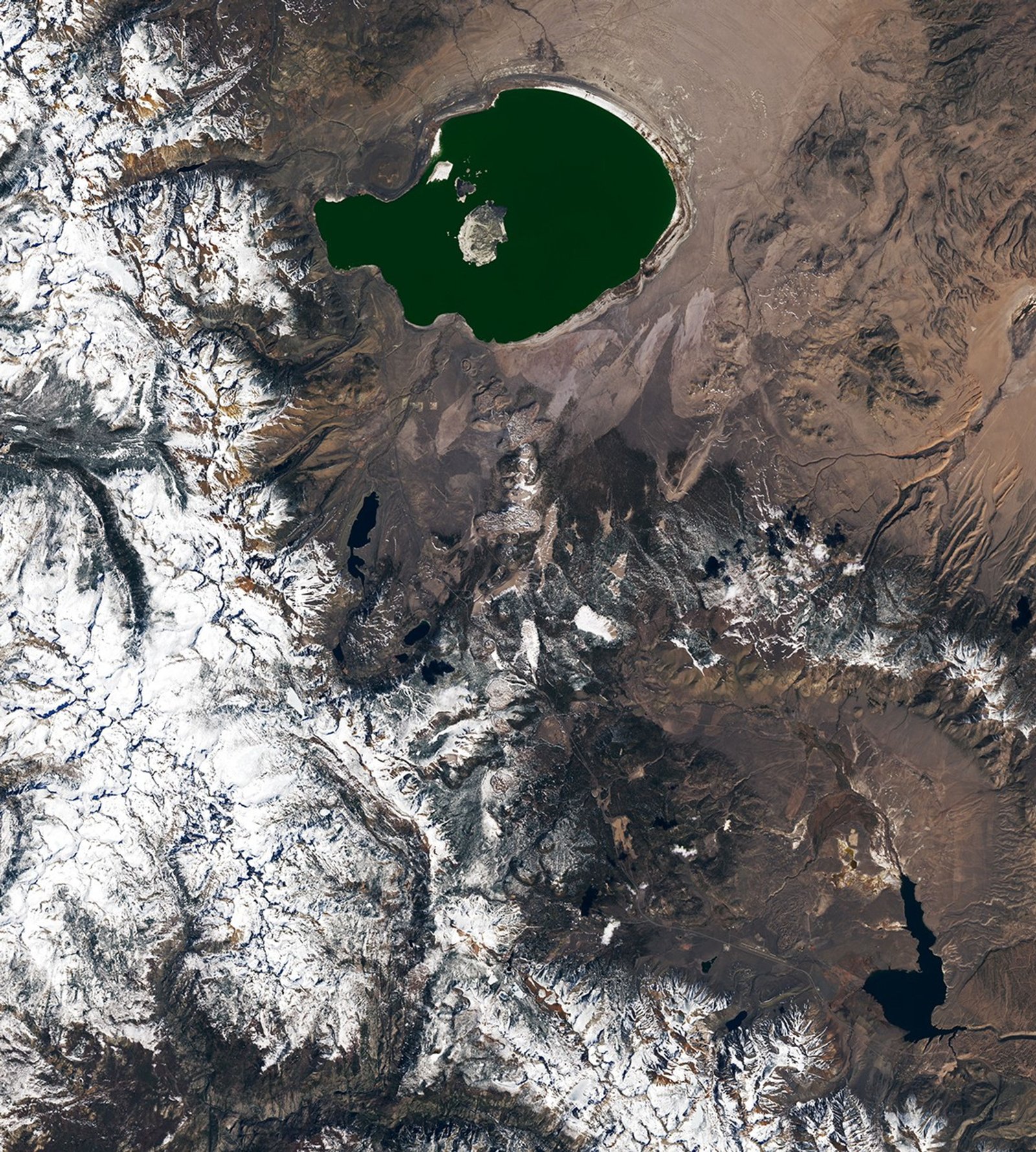 A string of small, partially snow-covered volcanic craters runs north-south between Mono Lake and Mammoth Mountain. Snowy mountains fill the left side of the image.
