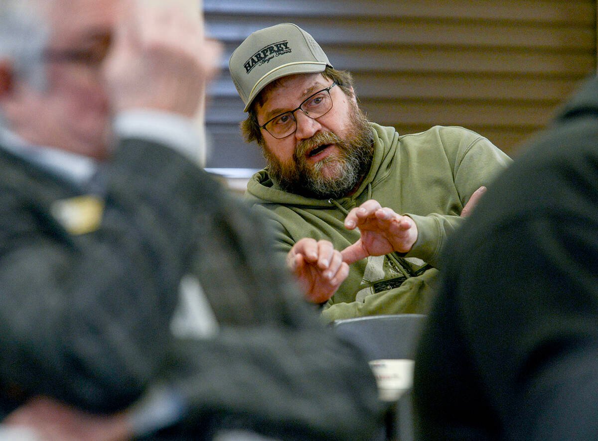 Mark Goetz, a bearded man with dark brown hair, dressed in an army-green sweatshirt and ball cap, gestures with his hands while discussing predation and exemptions to South Bruce’s dog bylaw for working livestock and herding dogs to an unseen person. Photo: Diana Martin.