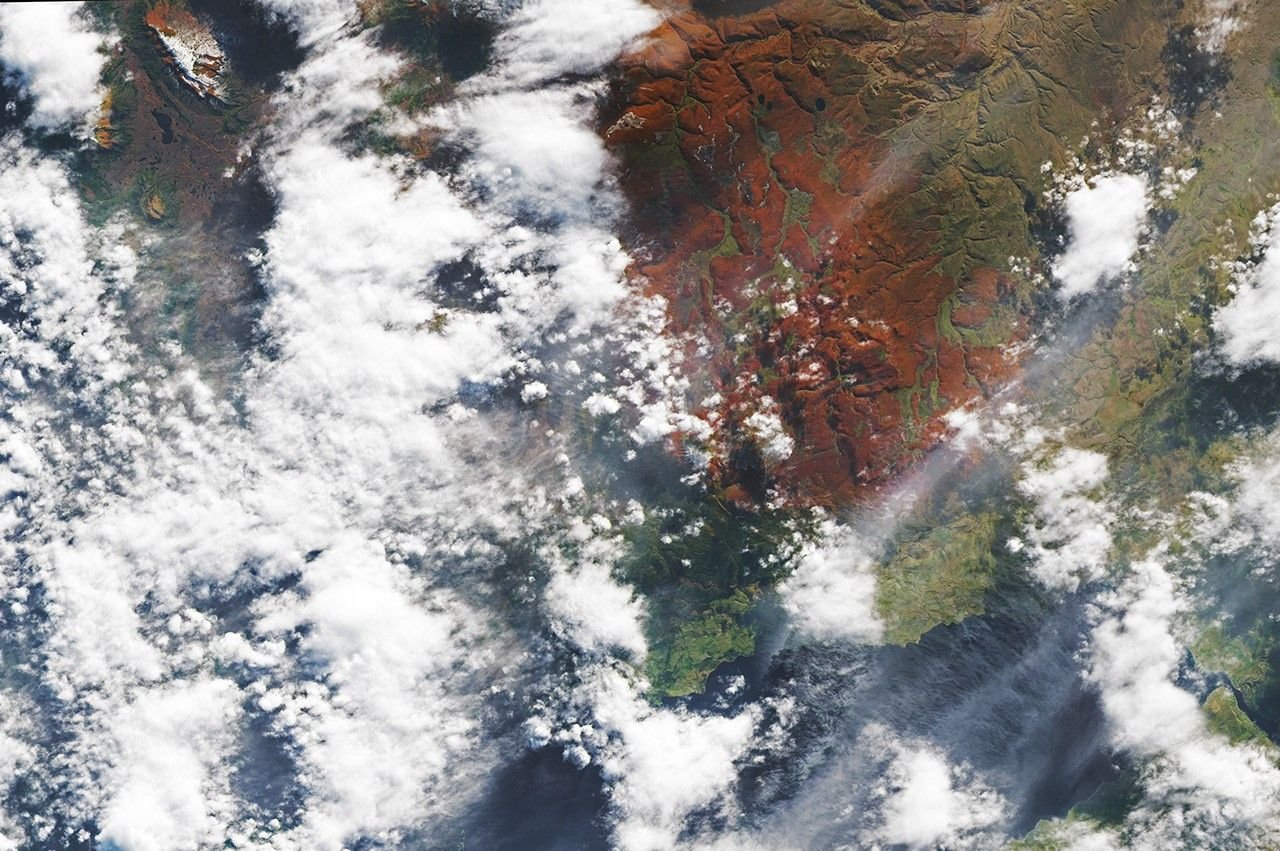 Hills tinged with reddish orange appear through a break in the clouds.