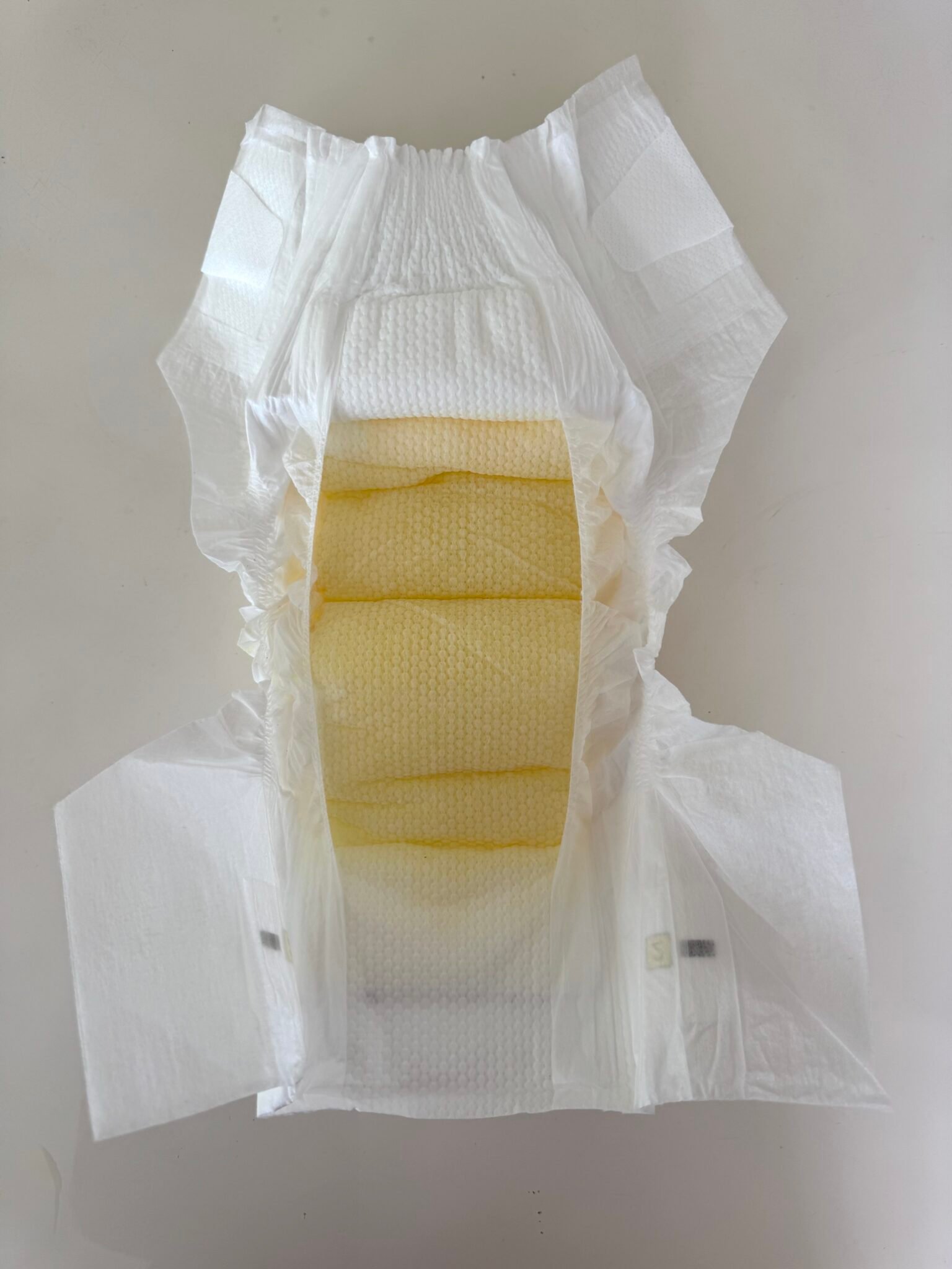 An open disposable baby diaper is lying flat, showing its absorbent yellow inner lining and elastic edges.