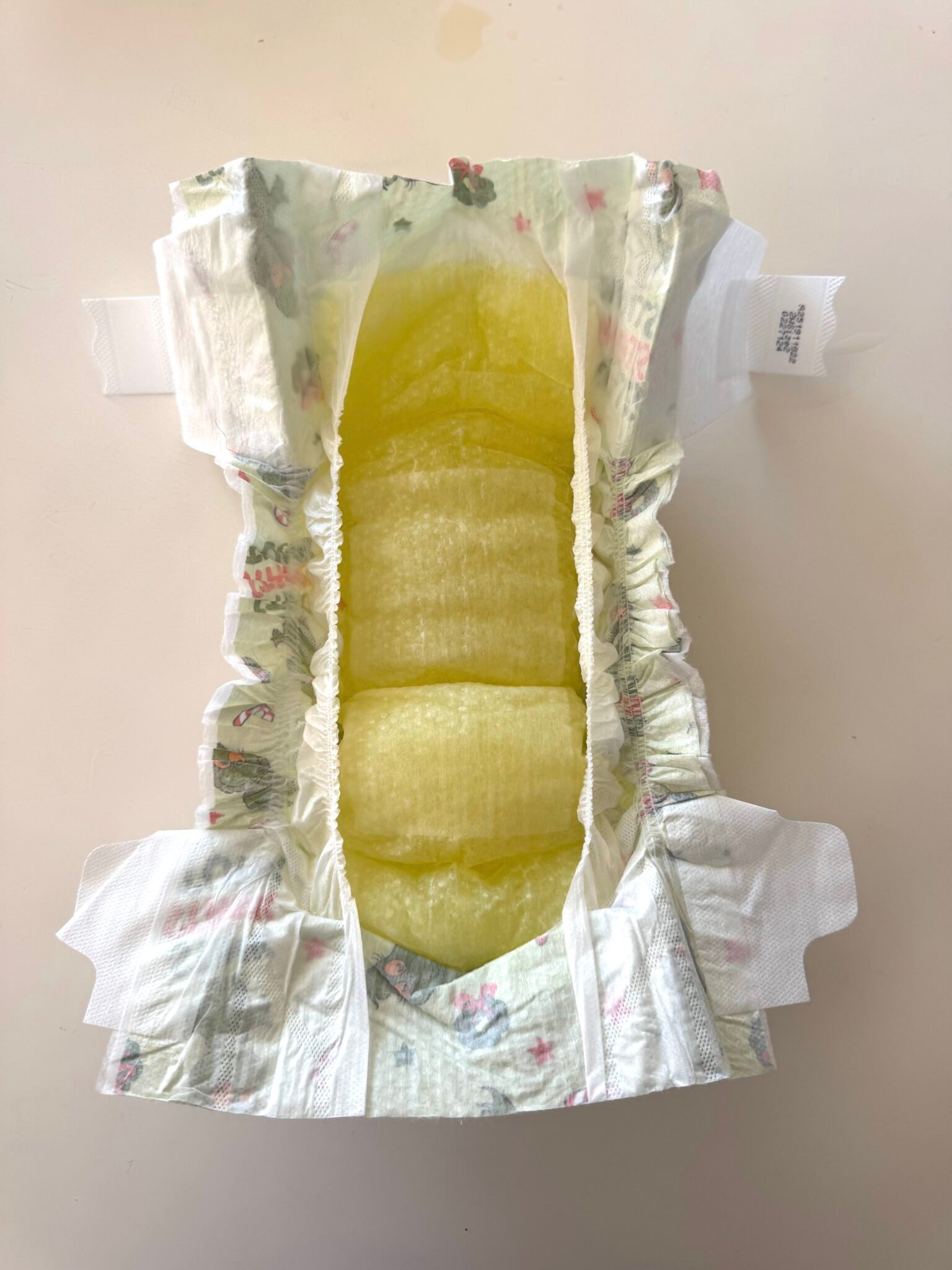An open disposable diaper on a flat surface, showing a yellow-stained absorbent area in the center.