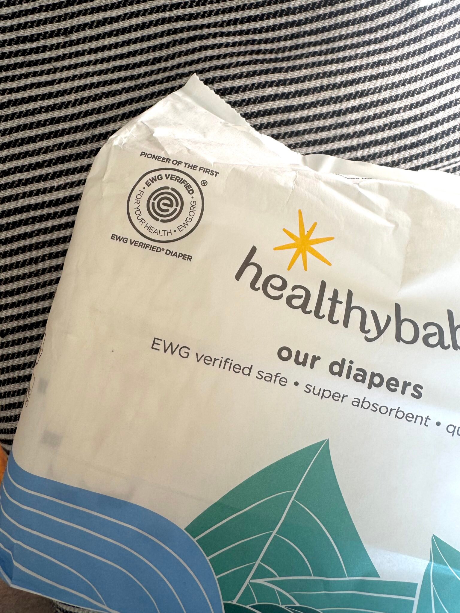 A pack of healthybaby brand diapers with EWG Verified and "for your health" logos on white packaging, placed on a striped fabric surface.