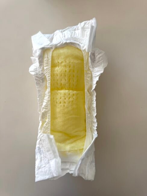 A disposable diaper lying open on a flat surface, displaying its yellow absorbent inner layer and elastic edges.