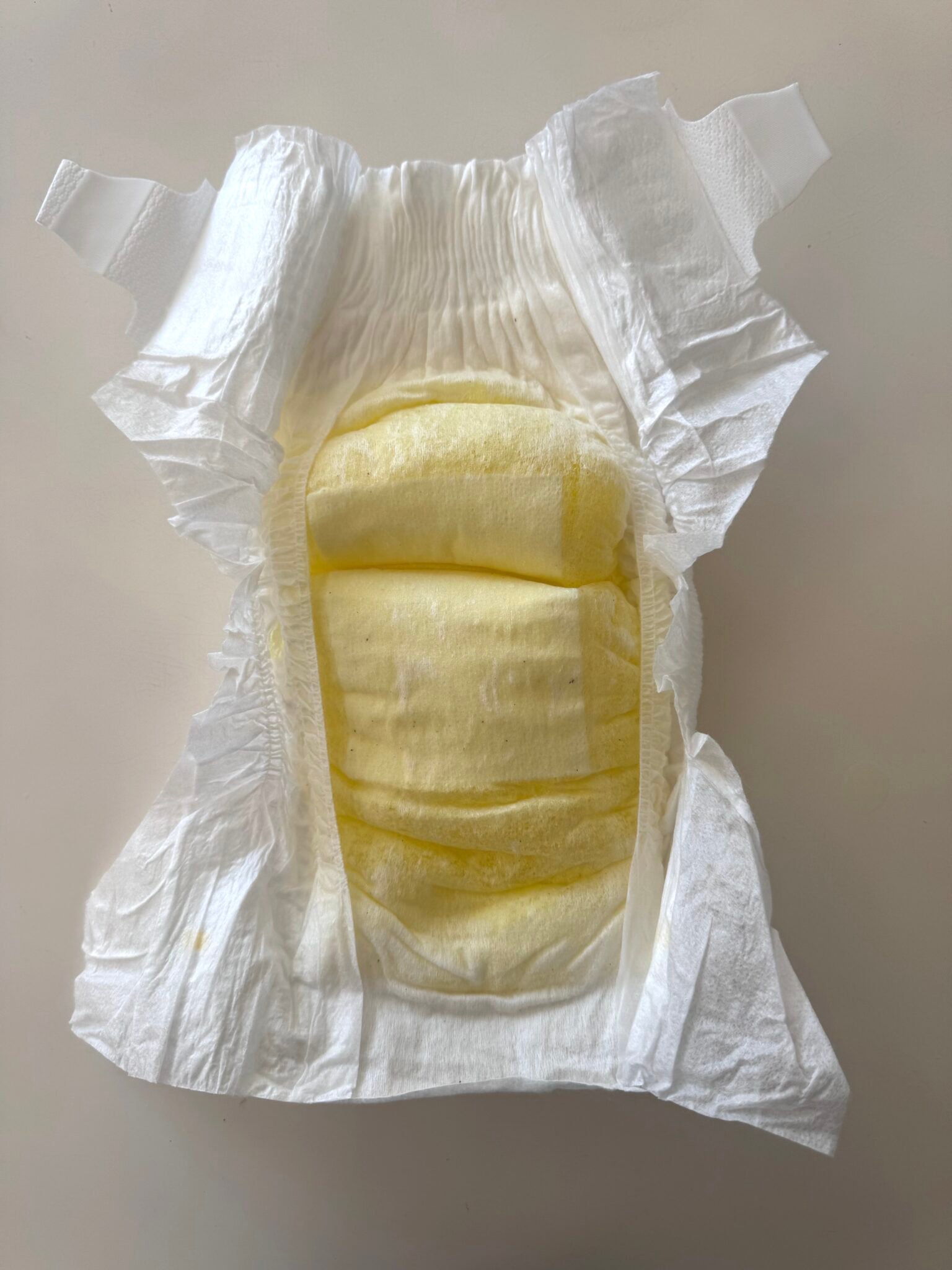 An unfolded disposable diaper with a yellow-stained absorbent pad, displayed on a flat surface.