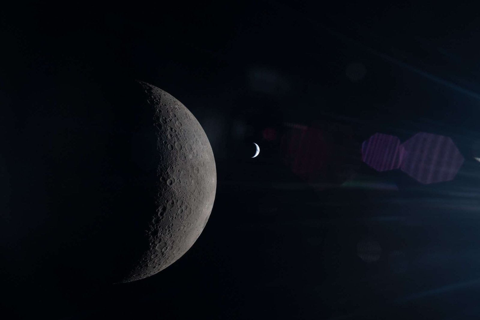 This image, taken from behind the Moon, shows its half-illuminated surface in sharp detail. To the right, a much smaller crescent Earth can be seen, with shades of blue and white just barely distinguishable. A faint reflection of the Orion spacecraft's window overlays the scene, especially in its right half.