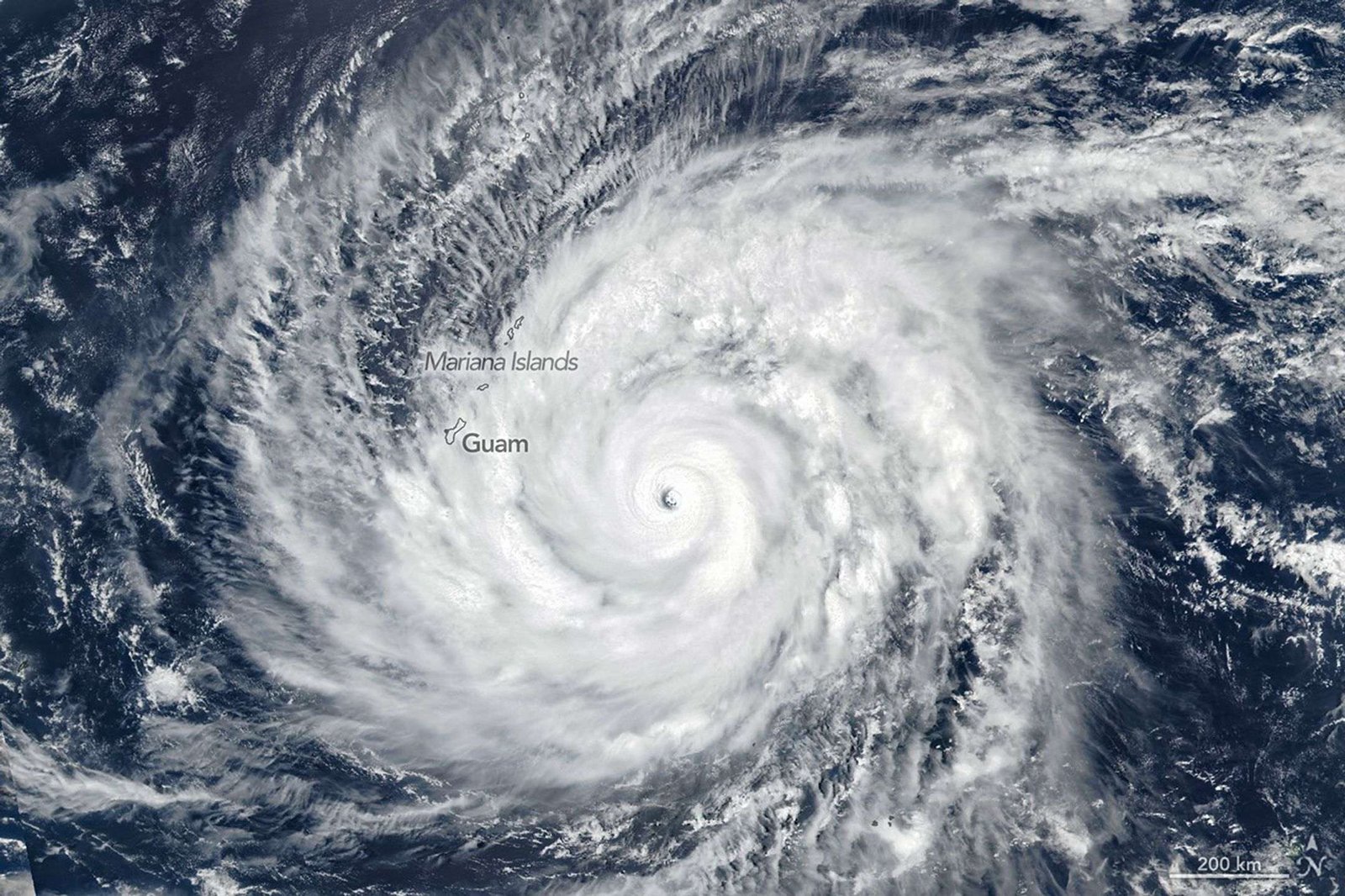 A large tropical cyclone spins over blue ocean water, its bright white cloud bands extending across parts of the Mariana Islands.