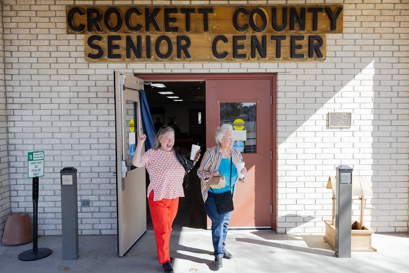 Two older women walk gleefully out of a building labeled Crockett County Senior Center