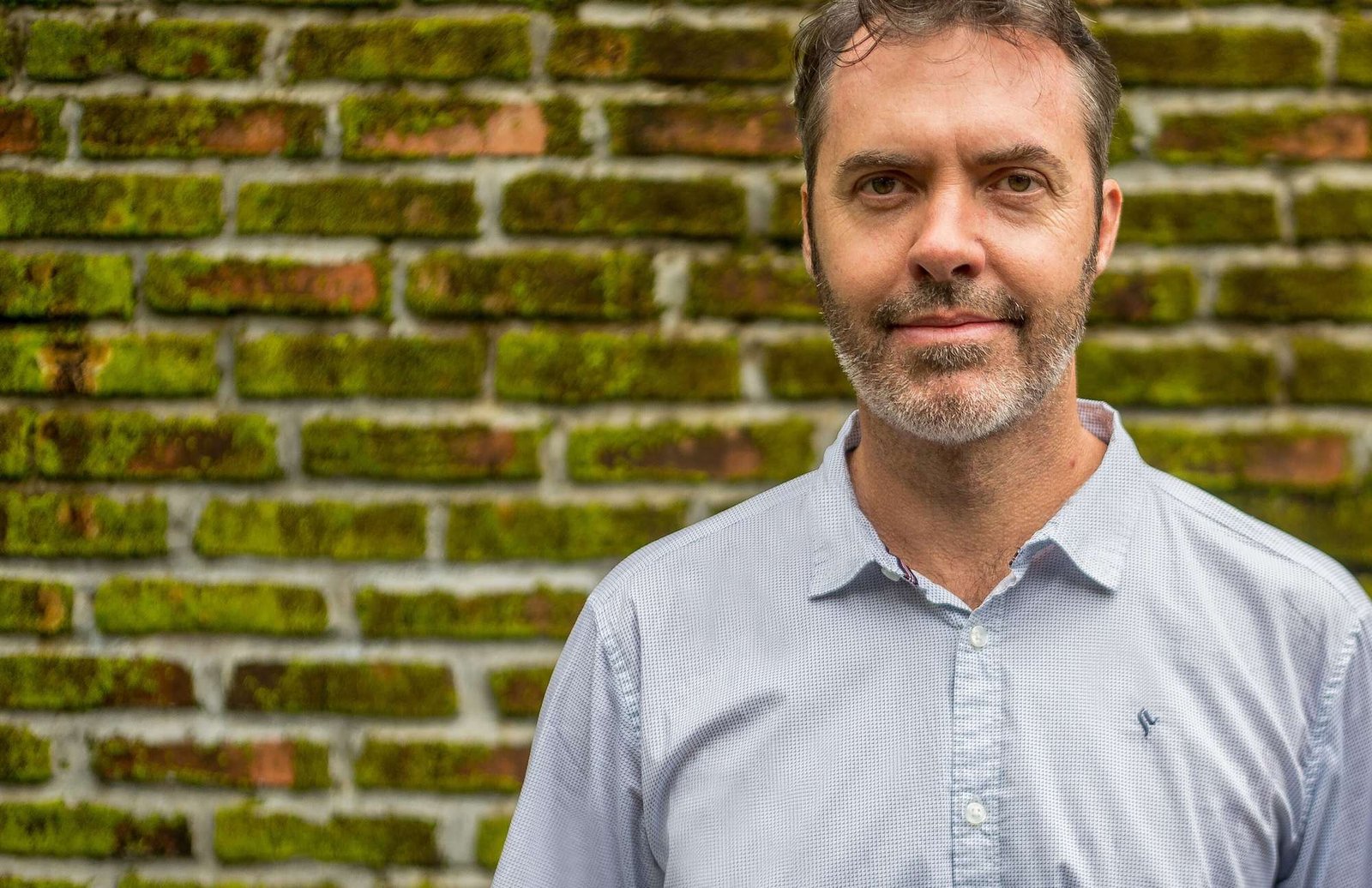 A middle-age man stands in front of a brick wall
