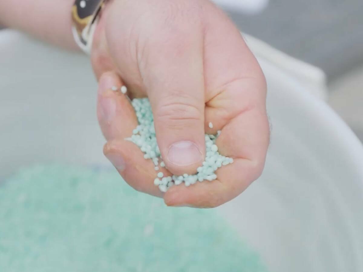 a hand holds light seafoam-coloured polymer-coated fertilizer pellets. Pic: Nutrien video screengrab via YouTube