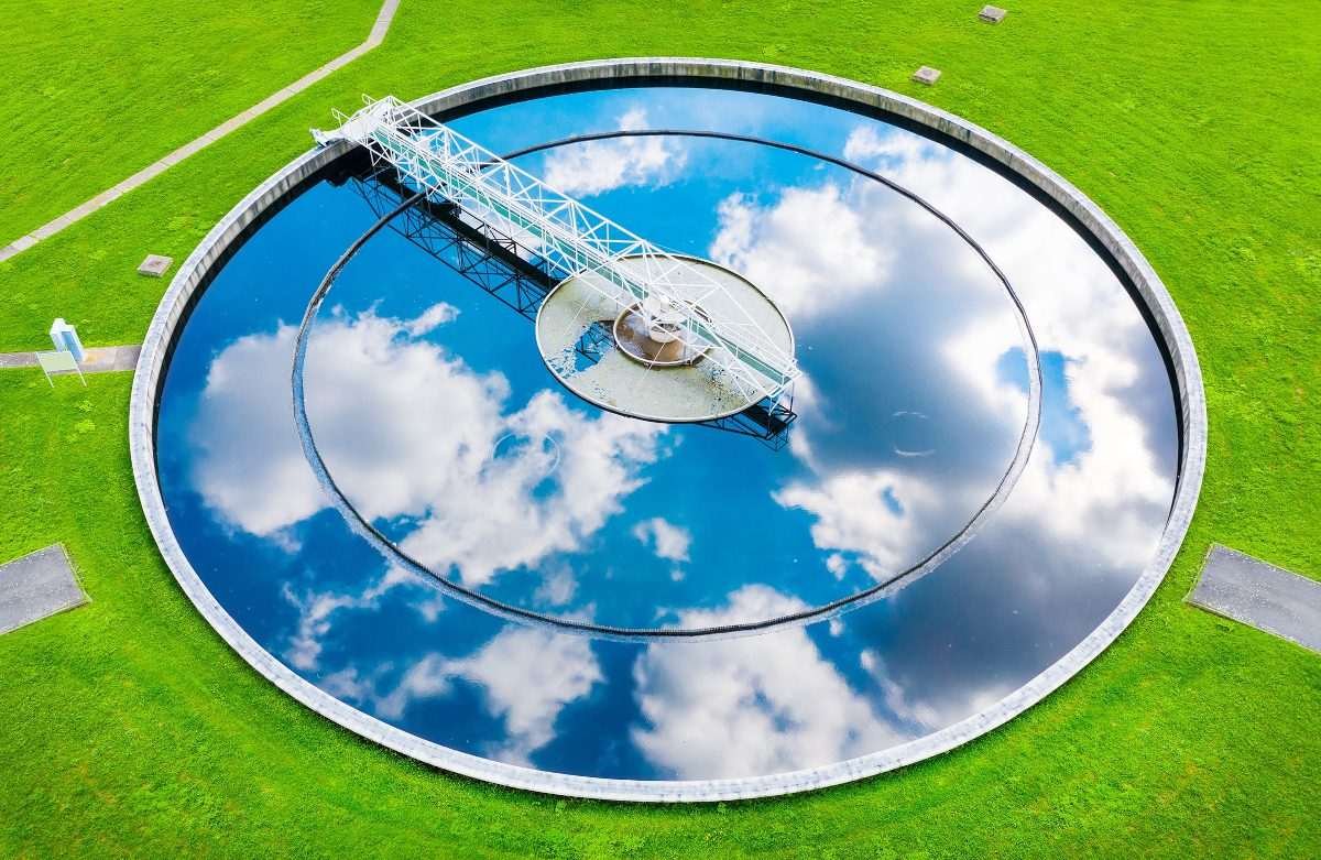 Wastewater clarifier tank seen from above with blue sky and clouds reflected on the surface of the tank's water