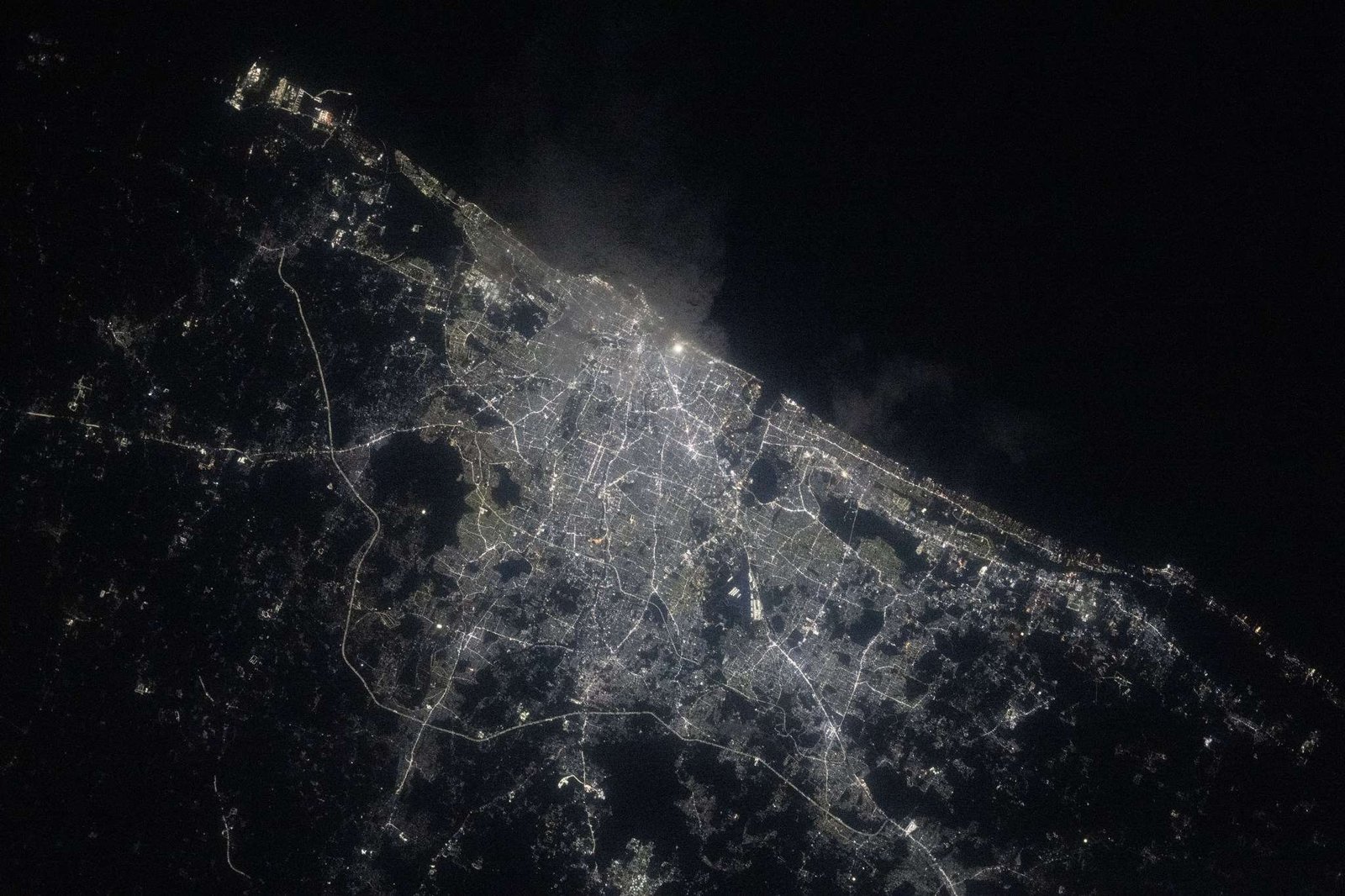A view of Chennai at night from the International Space Station shows a sprawling city along the water (upper right). City lights make the city shine while also highlighting roadways. The surrounding area is mostly dark.