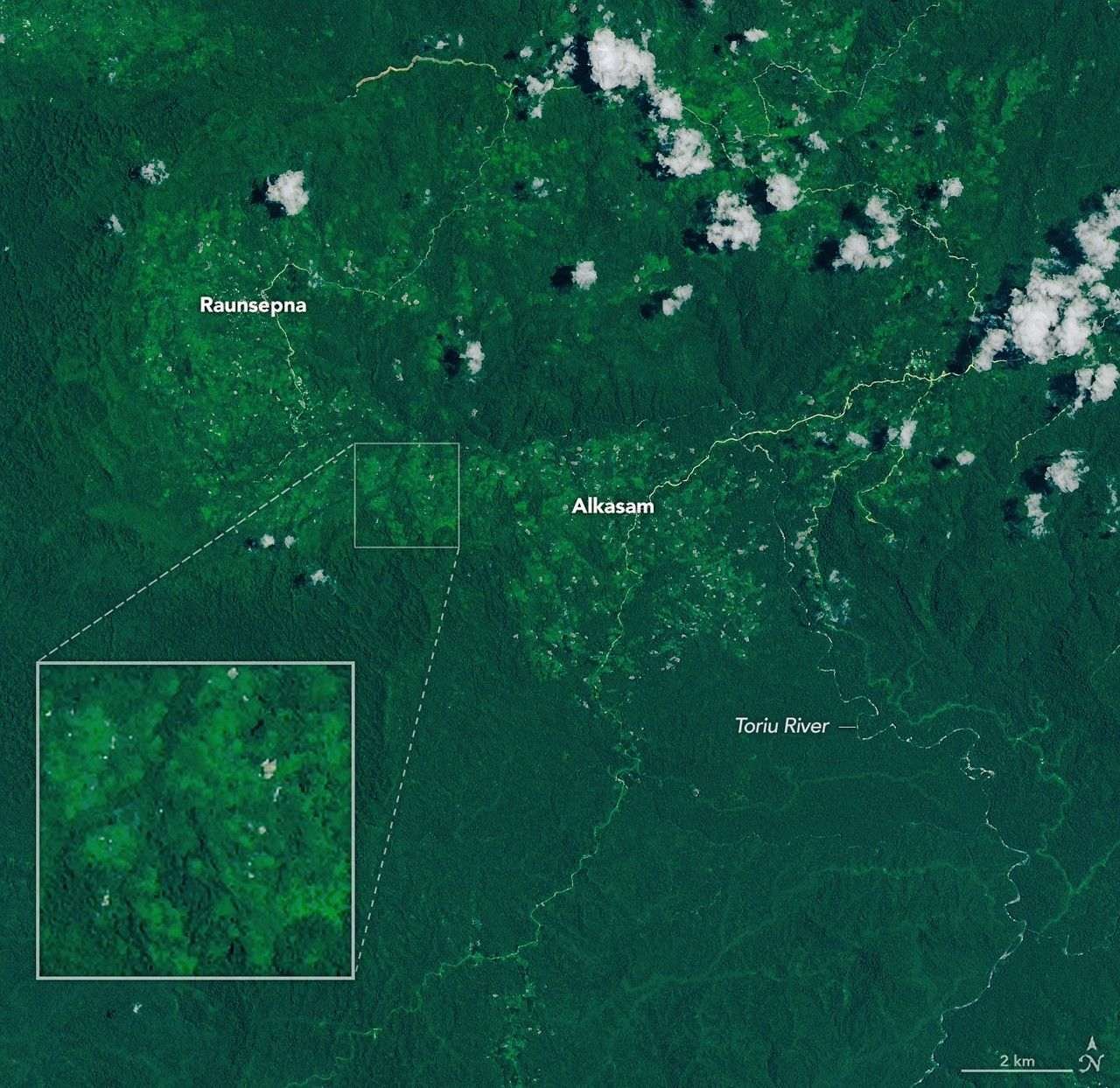 A narrow, light-brown landslide scar cuts through dark green forested mountains in East New Britain and extends south toward a stream valley. Rivers swollen with floodwaters, areas of forest clearing, and scattered clouds are also visible in some parts of the image.