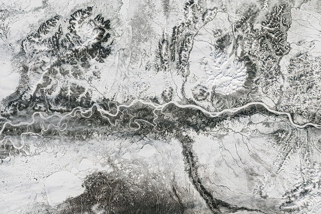 A frozen river winds from east to west past Aniak, Alaska. Nearby meandering channels are also frozen, and much of the surrounding land is snow-covered.
