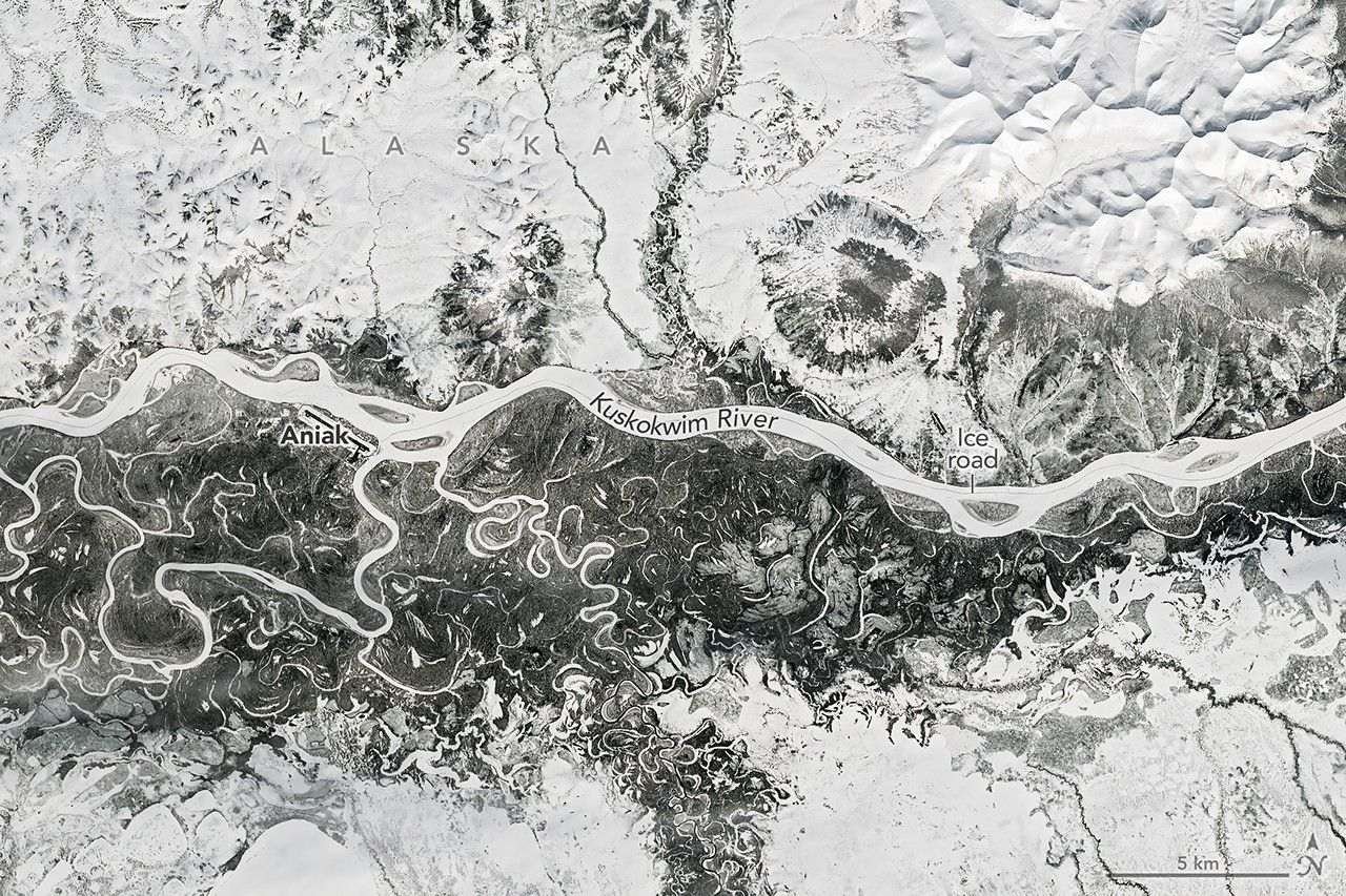A frozen river winds from east to west past Aniak, Alaska. Nearby meandering channels are also frozen, and much of the surrounding land is snow-covered.