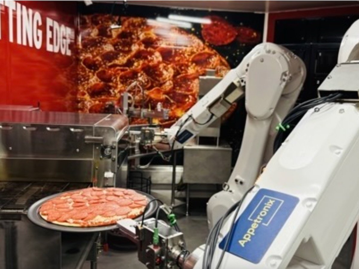 robot arms hold onto and work on an uncooked pepperoni pizza