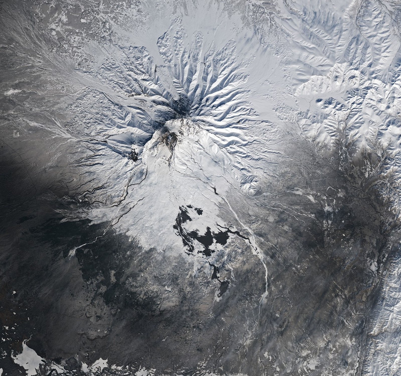 Dark channels and volcanic deposits are visible on the slopes of the snow-covered mountain.