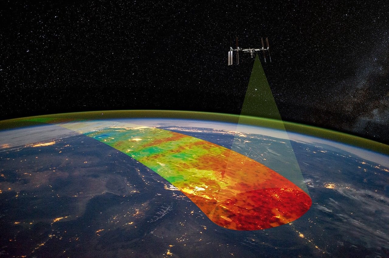 An artist's concept shows the International Space station in orbit above the nighttime side of Earth, with city lights visible on the planet and a band of green airglow wrapped around Earth's limb. A transparent cone extends downward toward Earth, representing AWE's field of view. A swath of color extends across Earth, representing the path of observations AWE has made in Earth's airglow during its orbit.