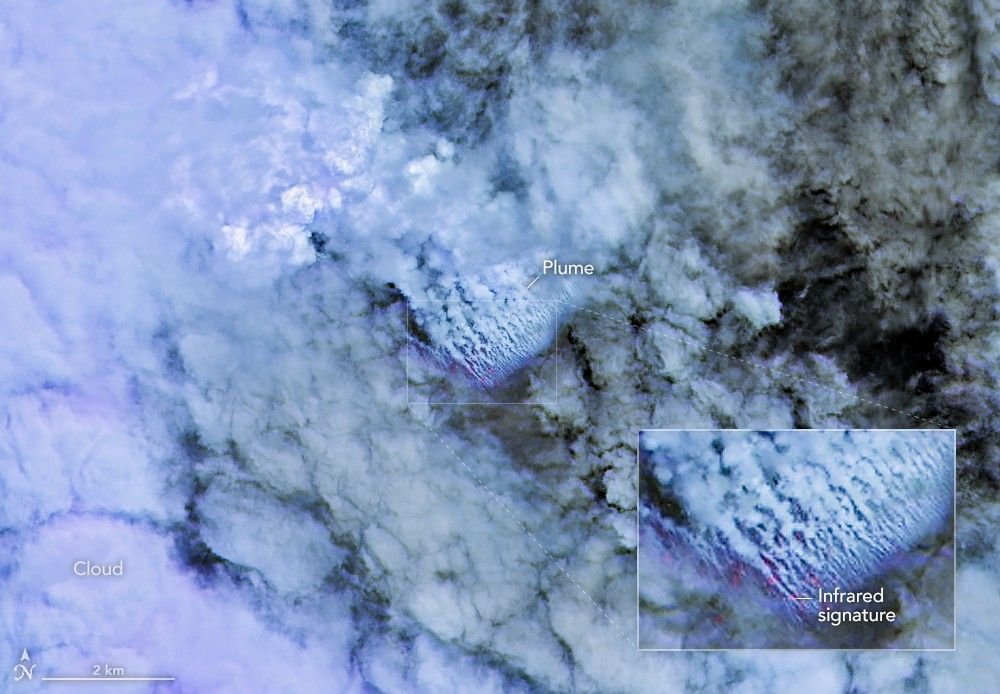 Only small patches of the ocean are visible through puffy, white volcanic plumes streaming from the center of the scene. Clouds not directly related to the eruption are visible throughout much of the image.  A false-color inset box shows the infrared signature of the eruption as a series of red dots near the volcanic plumes.