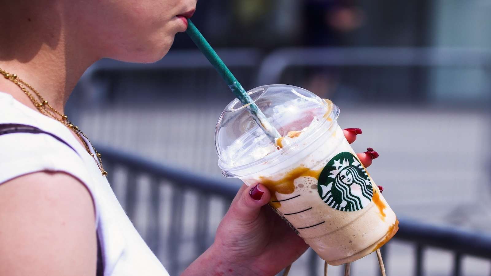 A person drinks a frozen Starbucks drink with a green straw