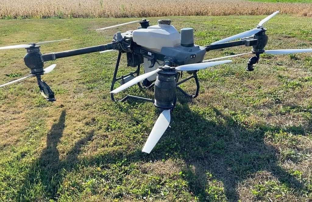 A DJI T100 drone with a chemical tanks sits on grass near a soybean field. Photo: John Greig