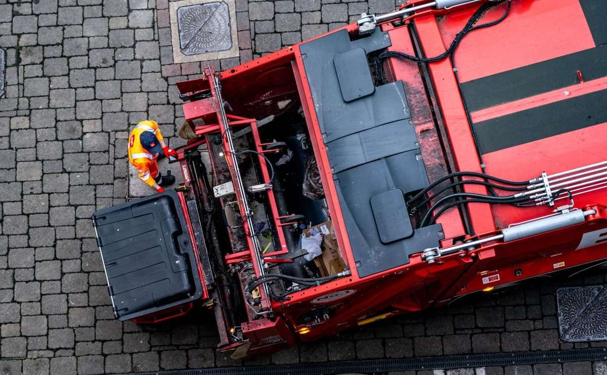 Aerial view of waste handlers loading bins into orange waste lorry