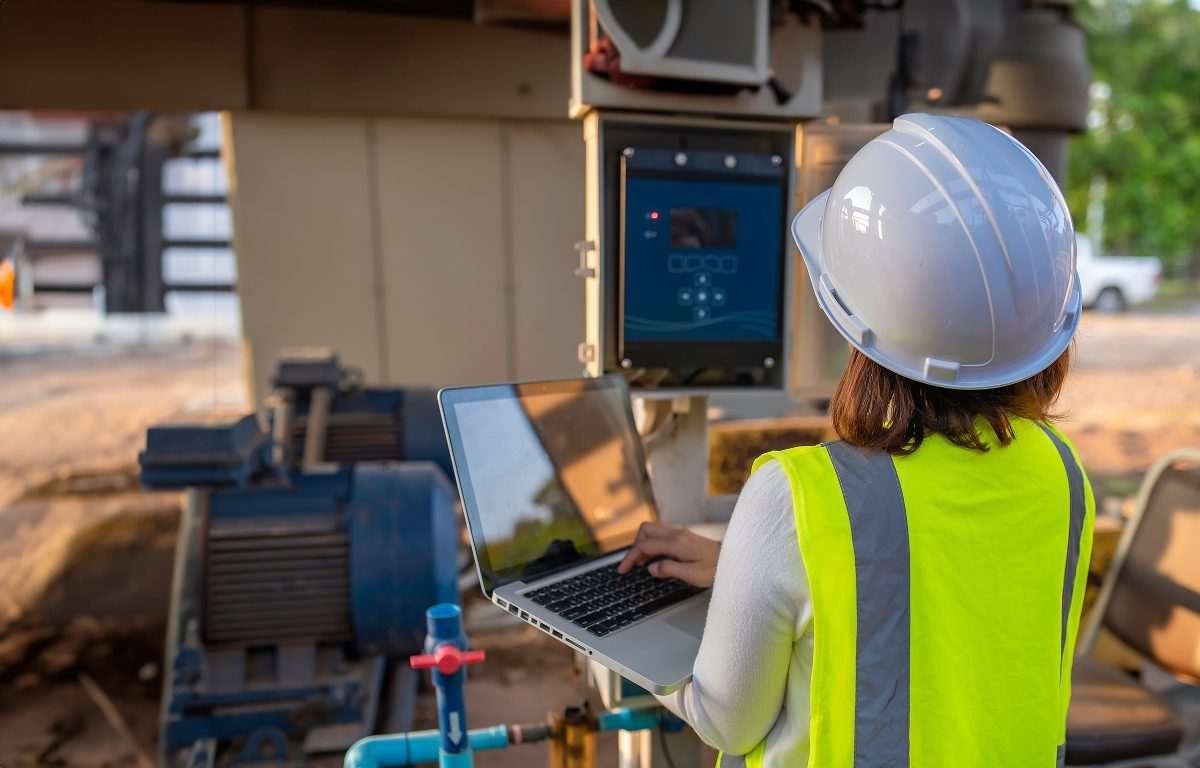 Engineer in safety equipment using a laptop beside industrial water infrastructure