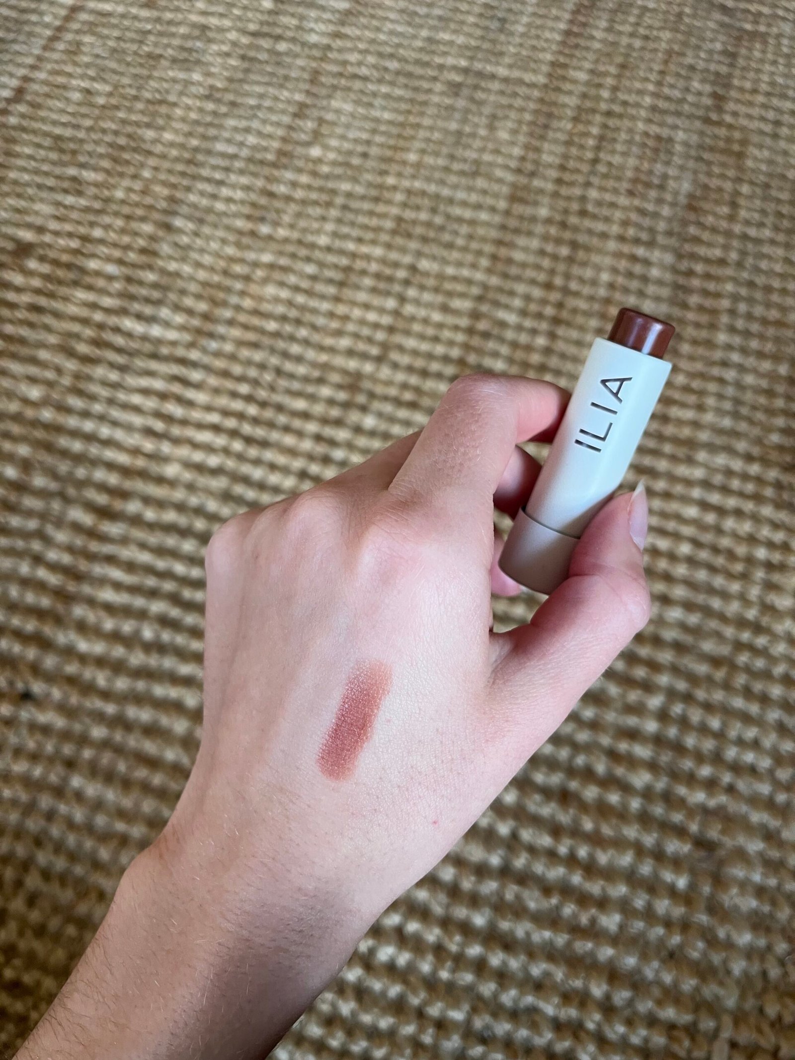 A hand holding Ilia Lip Balm