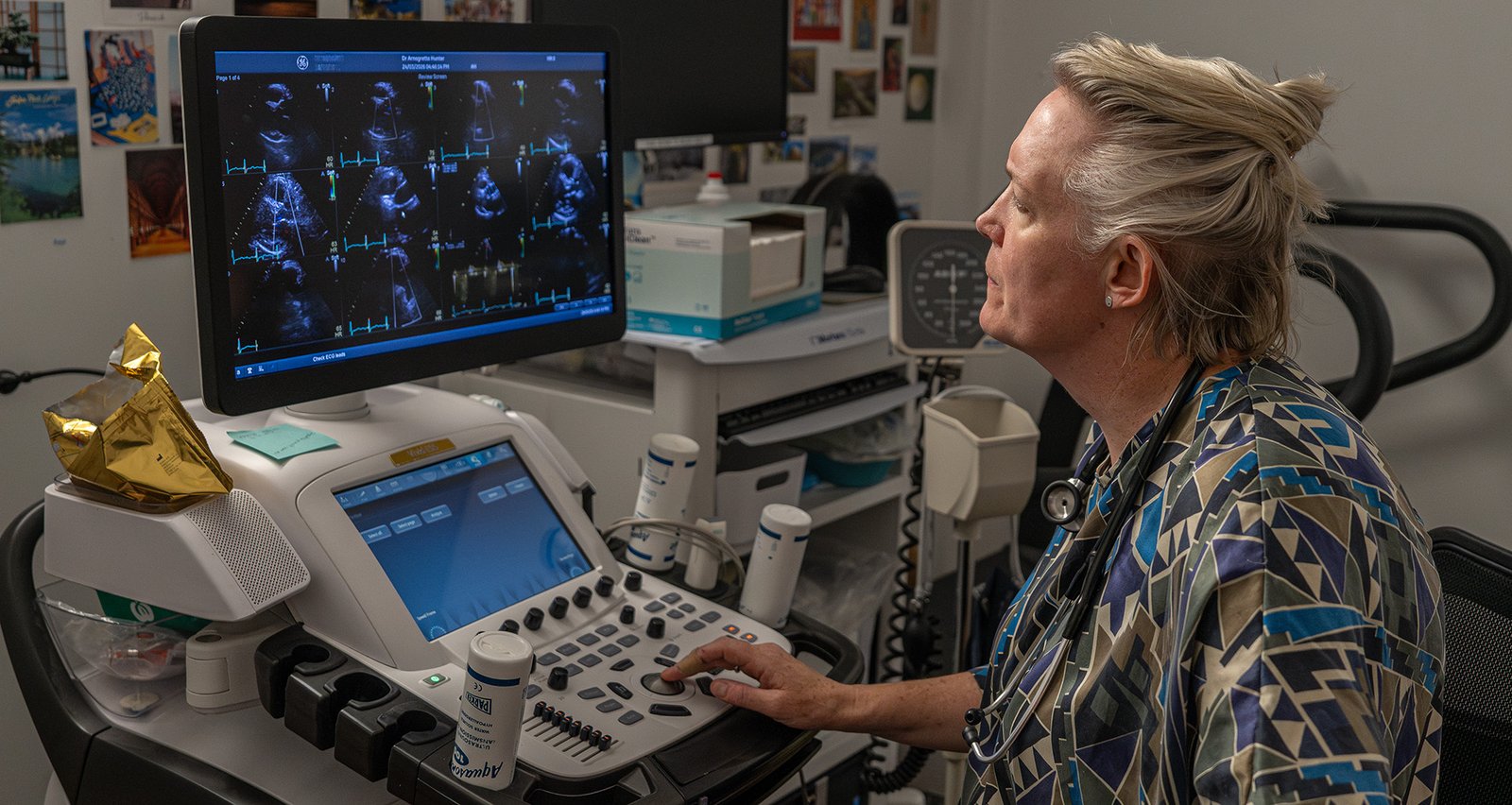 Arnagretta Hunter, wearing multicolored medical scrubs, sits in front of a computer screen displaying ultrasound images.
