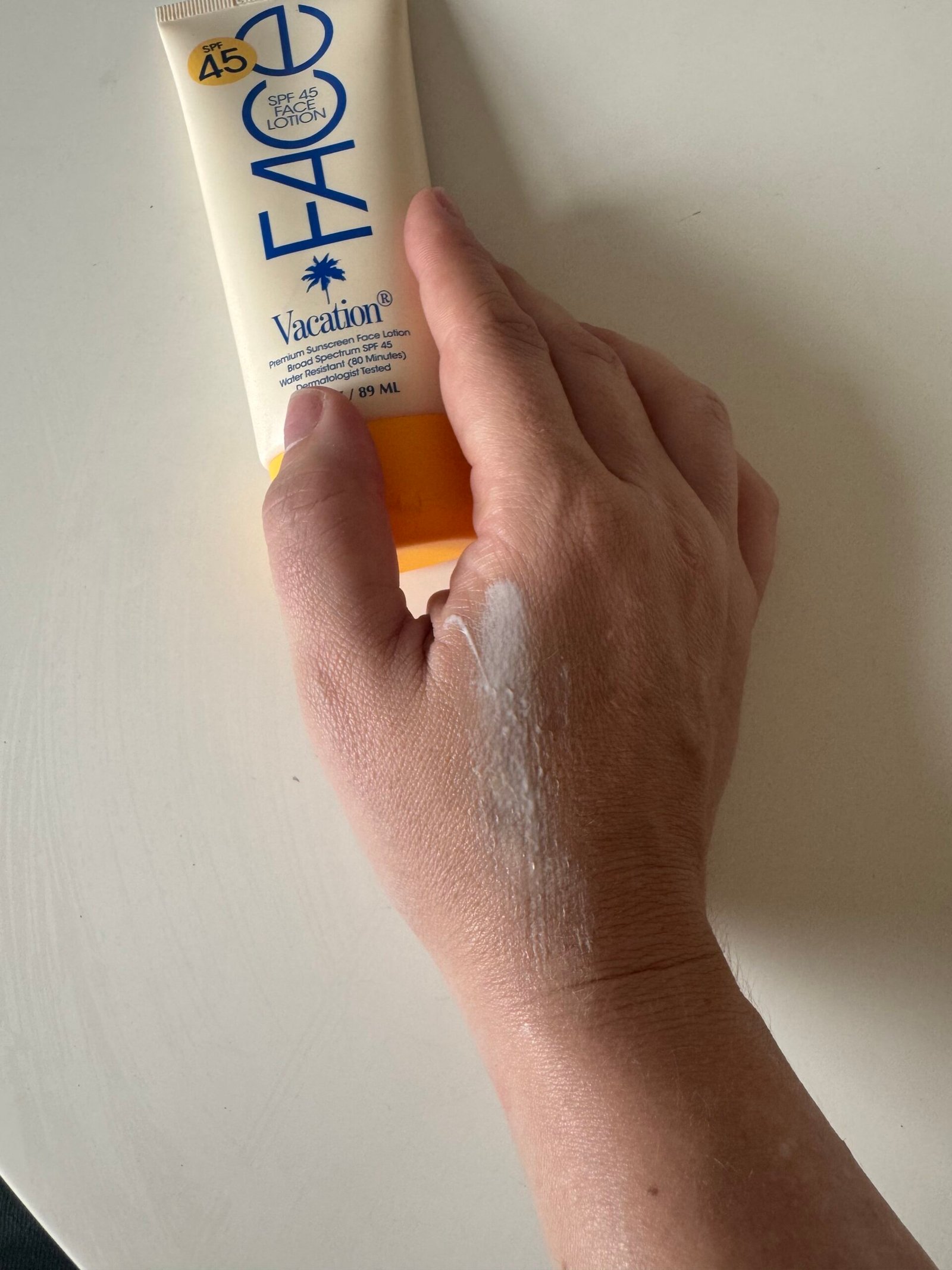 A hand with sunscreen lotion partially applied is shown next to a tube labeled "Vacation SPF 45 Face Sunscreen Lotion.