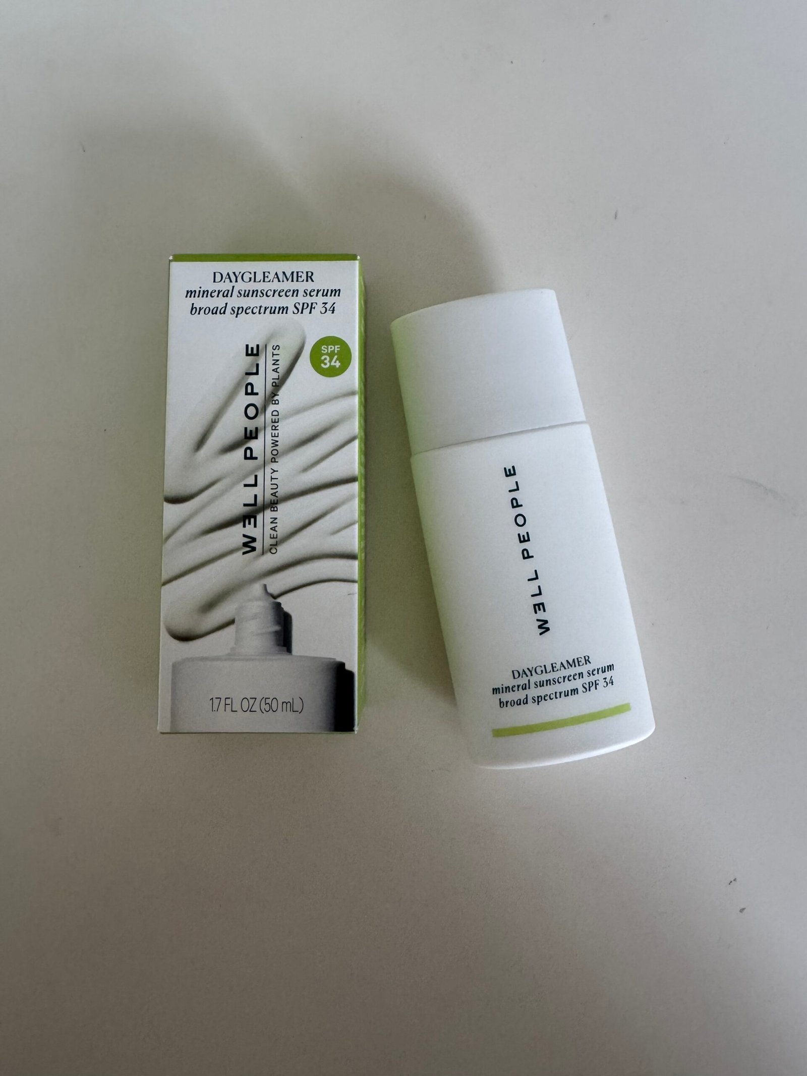 A bottle of Well People Daycleamer mineral sunscreen serum SPF 34 is shown next to its packaging on a white surface.