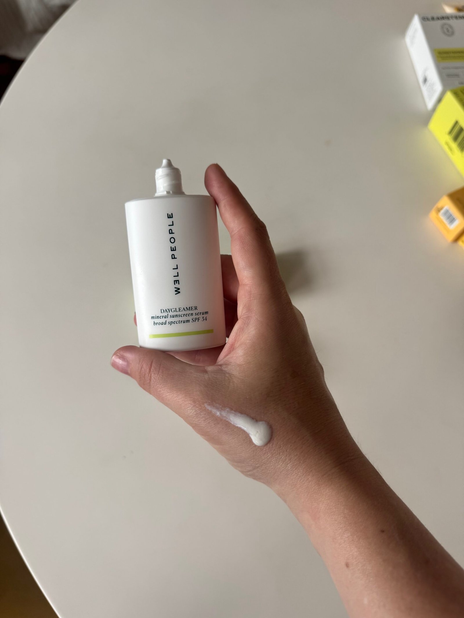 A hand holding a Milk People Daydreamer sunscreen bottle, with a small amount of sunscreen spread on the back of the hand.