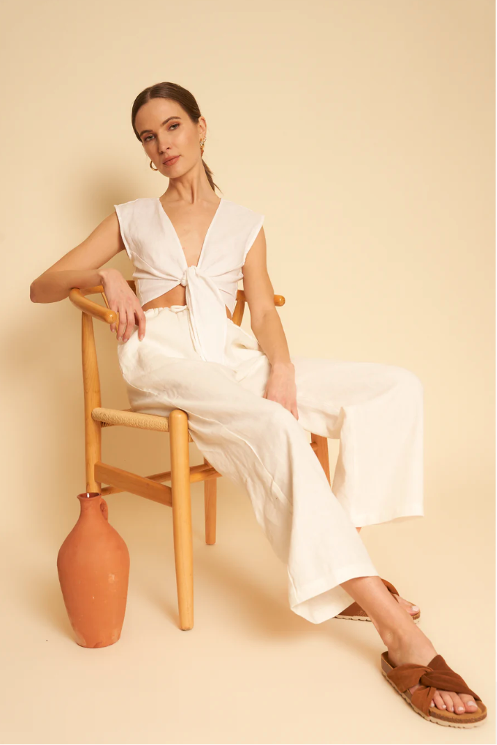 A model lounges in a chair, wearing a white linen set. 