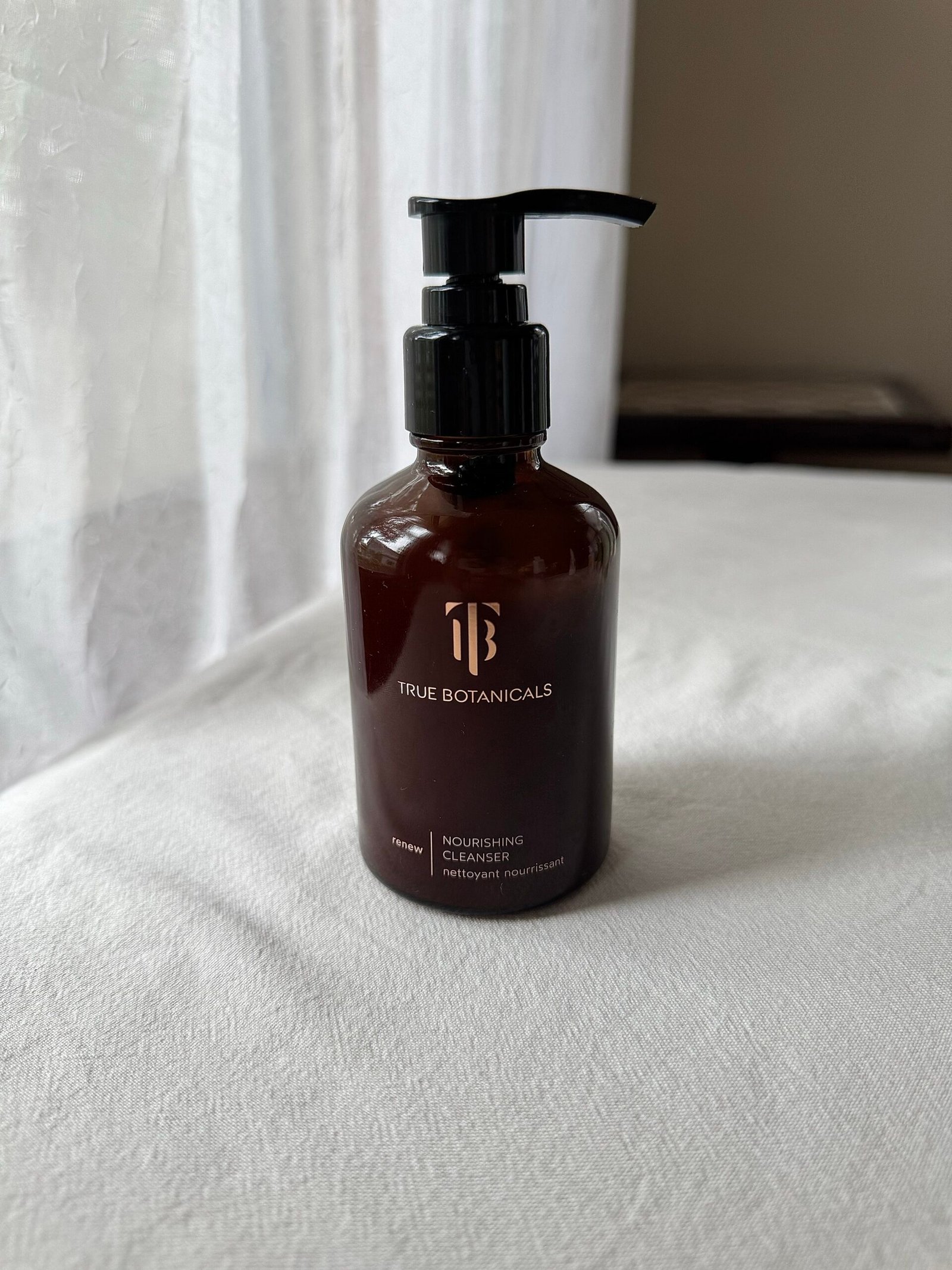 A bottle of True Botanicals face wash on a white fabric surface.