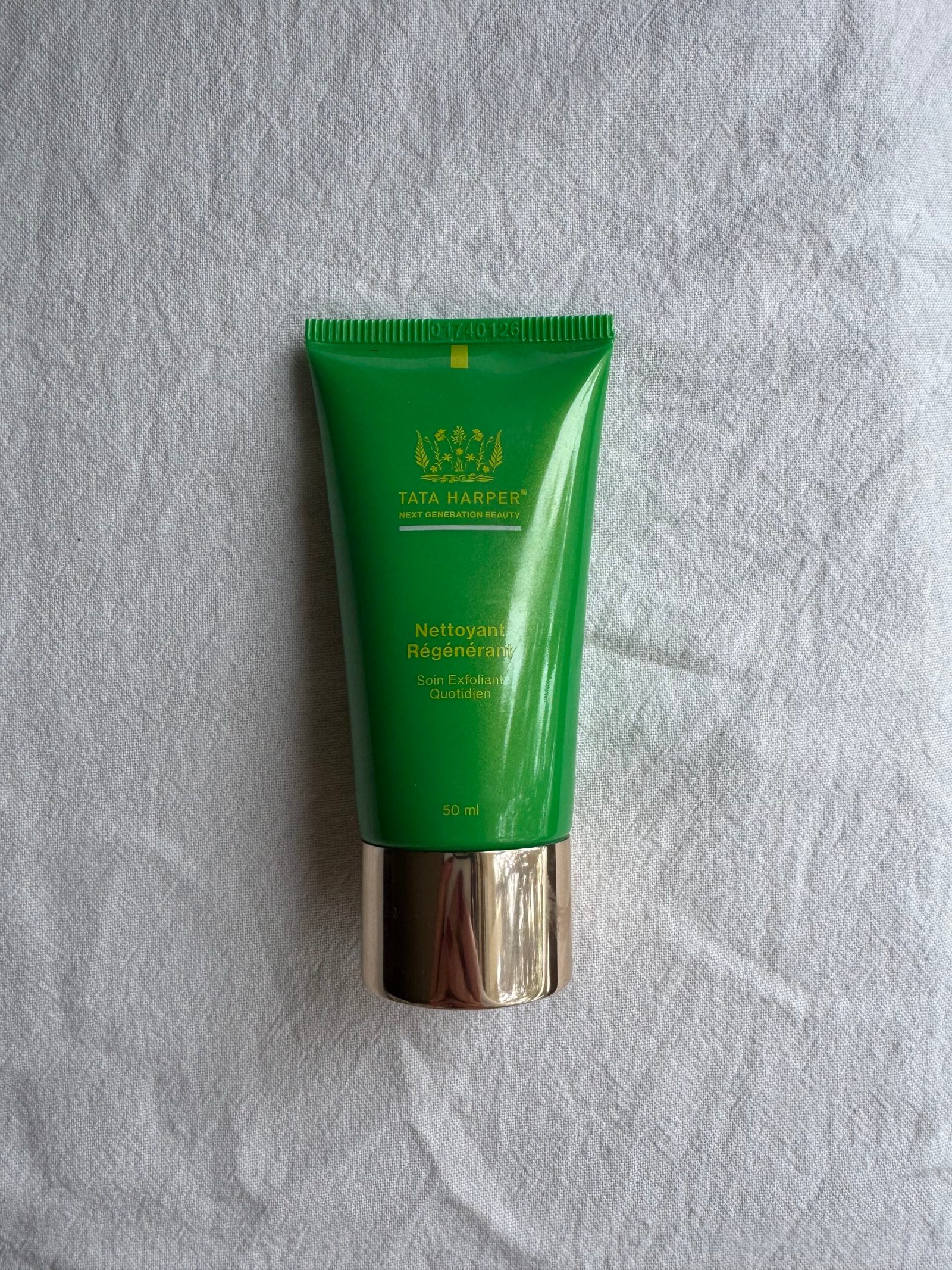 A tube of Tata Harper face wash on a white fabric surface.