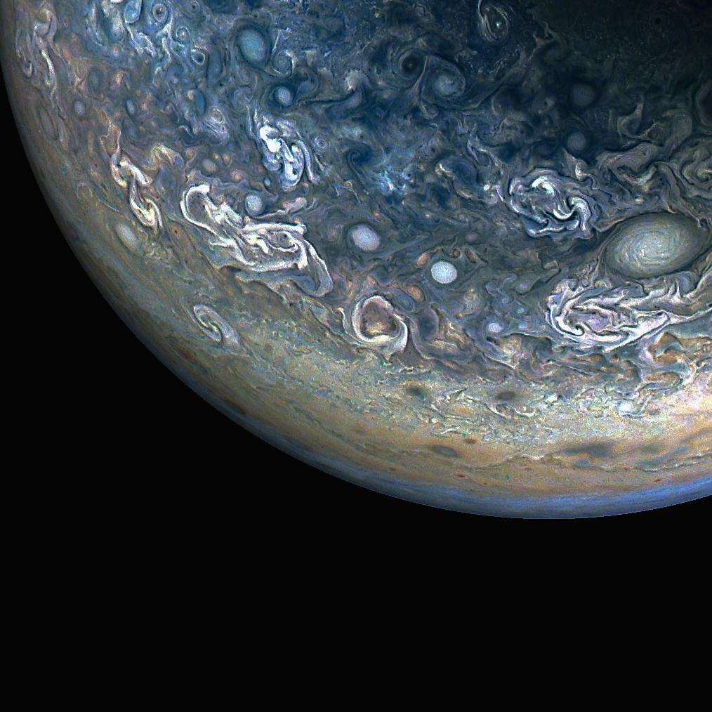 Three quarters of Jupiter can be seen in this photo; the darkness of space covers the bottom of the image. Green and blue swirls cover the planet's surface.