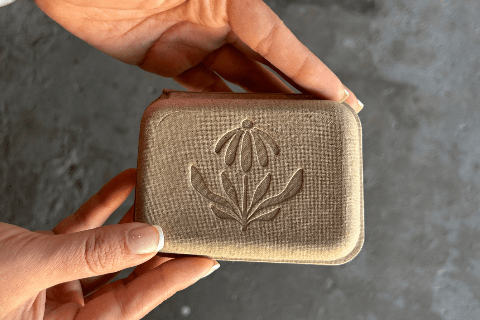 Molded pulp packaging box by s-packaging.com displayed upright on a natural stone, with embossed 'please reuse & recycle' text and leaf logo — eco-friendly sustainable packaging for brands