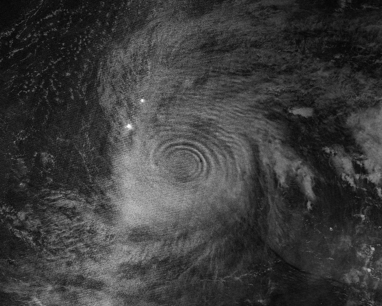 Gravity waves in the upper atmosphere appear as concentric rings in a nighttime, black and white satellite image. Clouds from a typhoon are also visible.