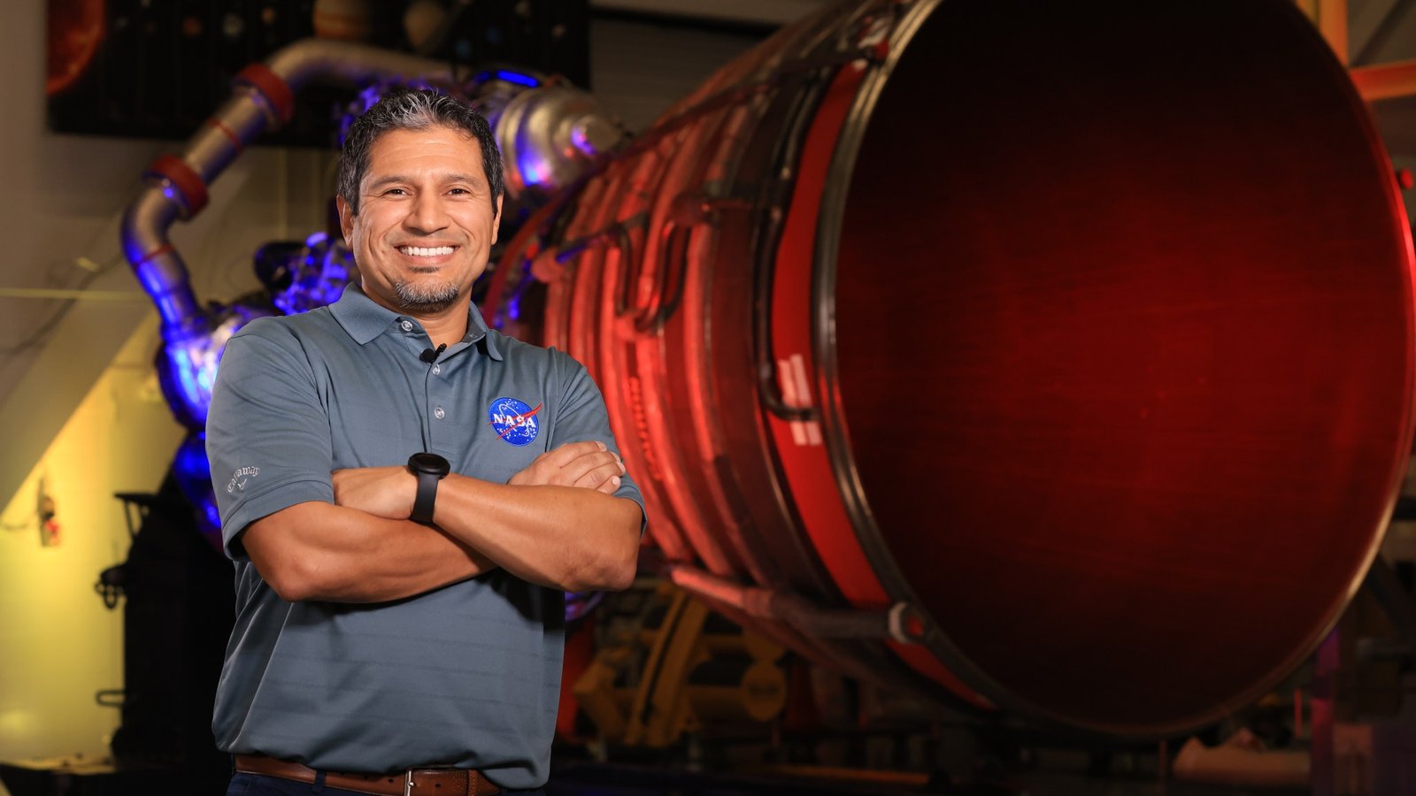 Elkin Norena, who serves as an SLS resident management officer at NASA’s Kennedy Space Center in Florida, stands in front of an RS-25 engine.