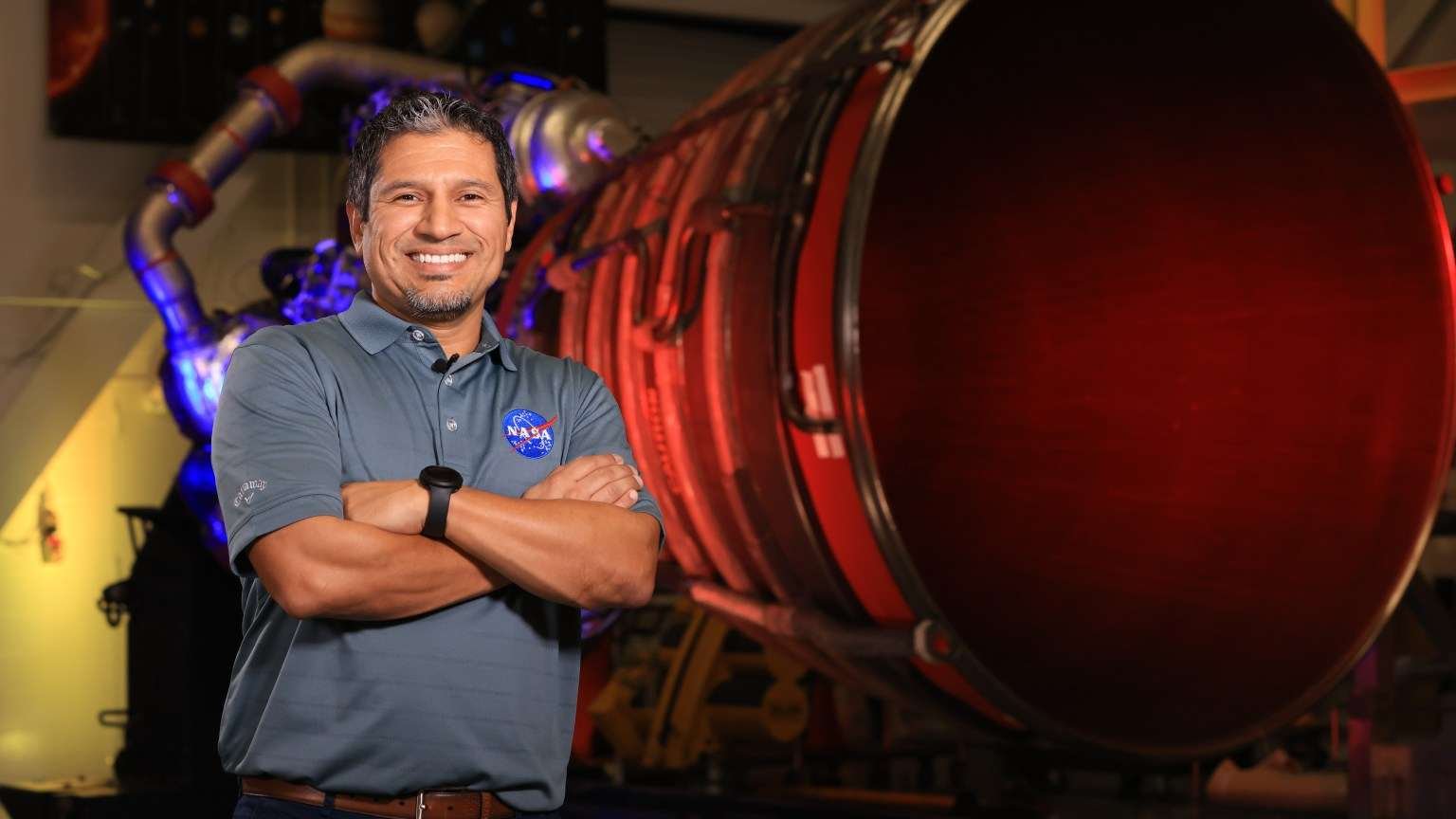 Elkin Norena, who serves as an SLS resident management officer at NASA’s Kennedy Space Center in Florida, stands in front of an RS-25 engine.
