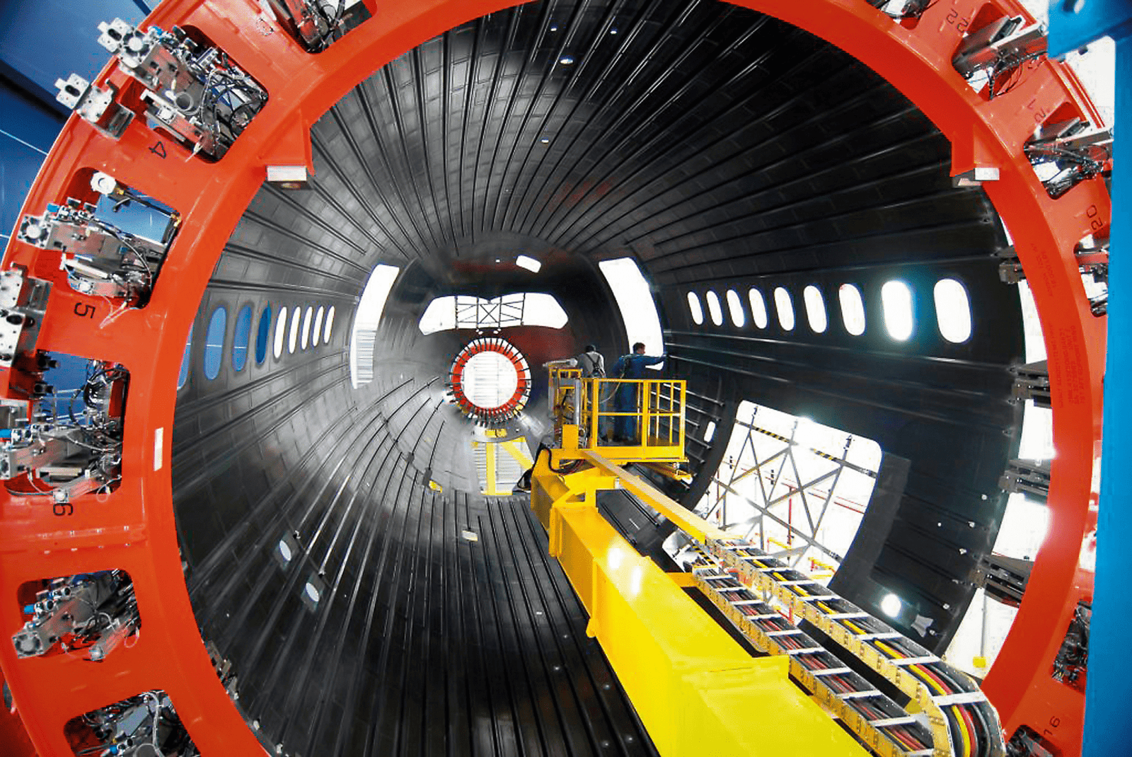 Large aircraft fuselage section under assembly inside a manufacturing facility as part of composite aircraft production work.