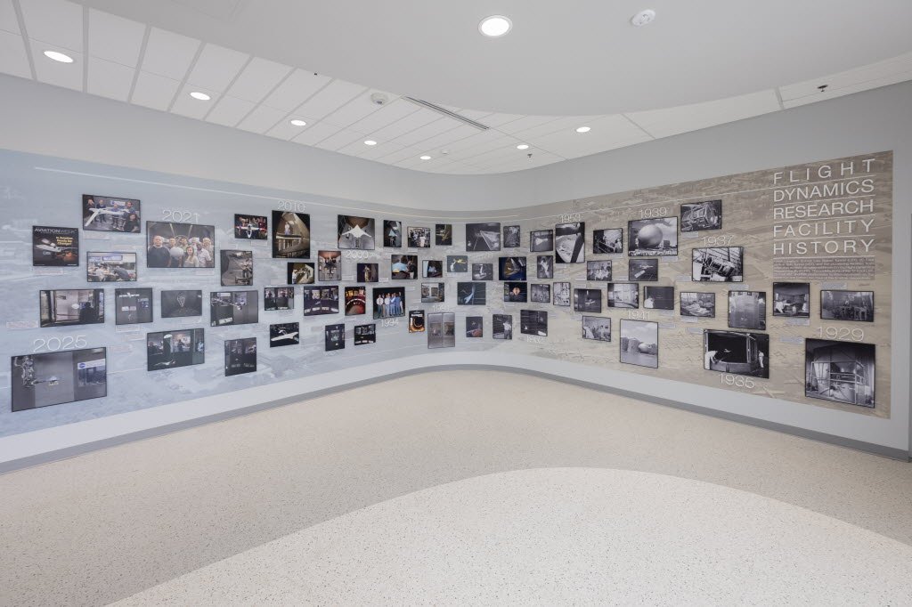 Pictures on a wall inside a facility with a sign that reads “Flight Dynamics Research Facility History.”