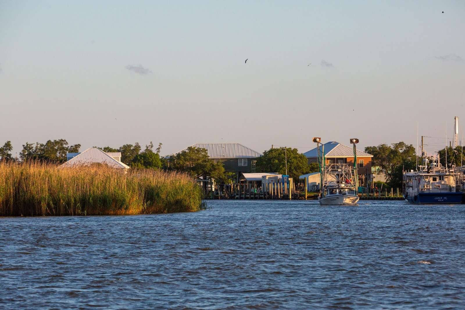 Fishing boats sit in the water in front of houses in the distance.
