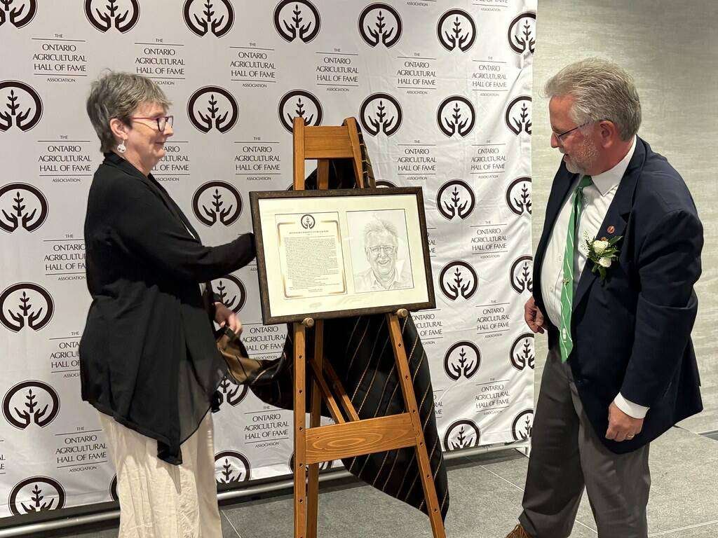 Senator Rob Black unveils his portrait at the induction ceremony with the help of board member Jean Howden. Photo: Ontario Agricultural Hall of Fame.