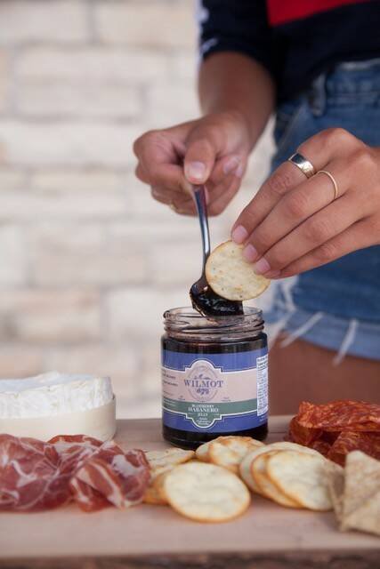 A hand spreads dark Wilmot Orchards jam onto a cracker beside a board of cheese and cured meats. Photo: Courtney Stevens